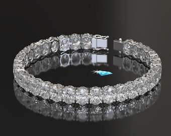 May include: A silver-toned tennis bracelet featuring a continuous row of oval-cut clear stones set in a metallic frame. The bracelet includes a secure box clasp mechanism and is displayed against a dark background with a small blue diamond icon.