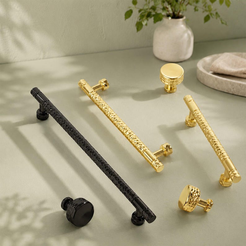 May include: A collection of cabinet hardware including two long bar pulls and two round knobs. One long bar pull and one round knob are finished in matte black, while the other long bar pull and round knob are finished in polished gold.