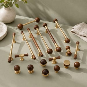 May include: A collection of cabinet hardware featuring a mix of brass and dark wood finishes. The set includes various lengths of drawer pulls, T-bar handles, and round knobs, all showcasing a combination of metallic gold-toned brass and wood.