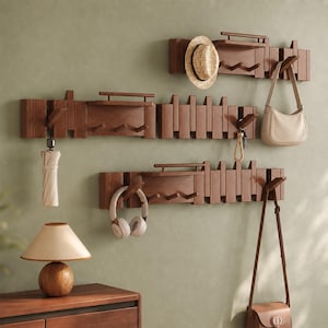 May include: Three horizontal wall-mounted wooden coat racks with integrated shelves and multiple angled hooks. The racks feature a slatted design and hold a straw hat, a beige umbrella, a beige handbag, white headphones, and a brown leather shoulder bag.