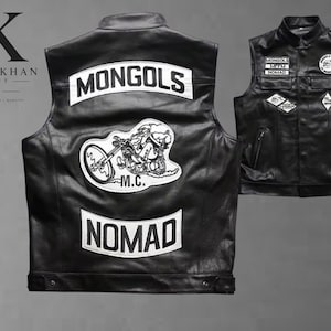 May include: A black leather vest featuring white embroidered patches. The back displays the text MONGOLS and NOMAD with a central graphic of a motorcycle rider. The front includes smaller patches with text and a circular emblem on the chest.
