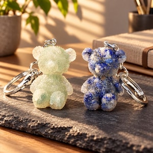 May include: Two bear-shaped keychains with textured, crystalline surfaces. One bear is a pale, translucent mint green, while the other features a deep blue and white marbled pattern. Both are attached to silver-toned metal split rings.