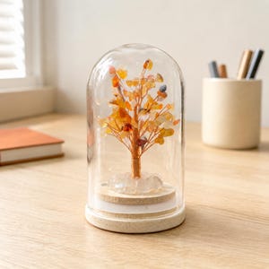 May include: A decorative tree sculpture made of copper wire and small orange, yellow, and clear gemstone chips, housed inside a clear glass dome with a round wooden base. The tree sits on a cluster of clear crystals atop the wooden platform.