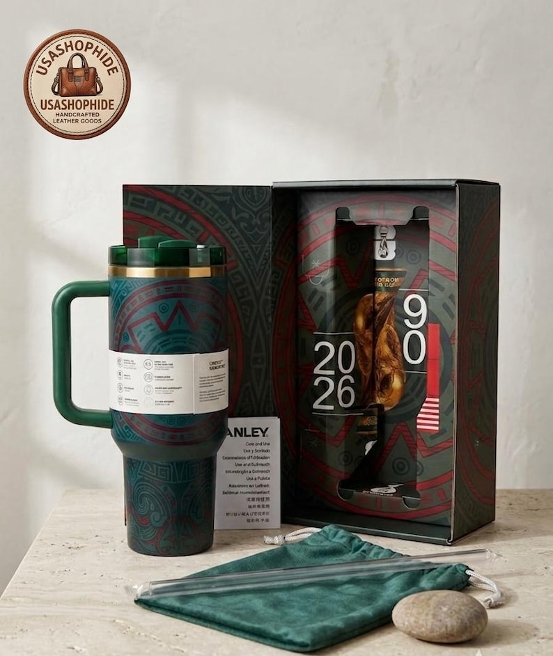 May include: A dark green insulated tumbler with a handle and a patterned design, featuring a matching gift box with the text 20 26, a green velvet pouch, and a clear straw. The tumbler has a white product information band wrapped around it.