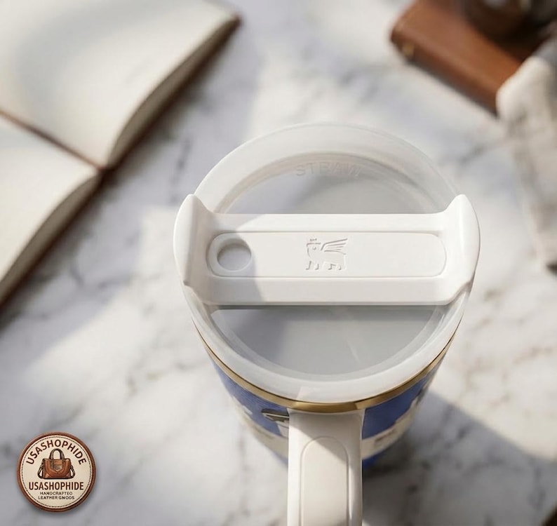 May include: A white plastic tumbler lid with a rotating closure mechanism featuring a circular straw opening and a small embossed winged creature logo. The word STRAW is molded into the top surface of the lid, which sits atop a blue vessel.