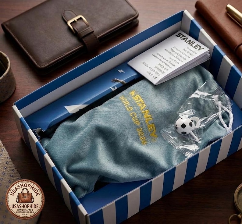 May include: A blue and white striped box containing a blue fabric pouch with the gold embroidered text STANLEY WORLD CUP 2026, a small white and black soccer ball charm in a plastic bag, and a white Stanley brand instruction booklet.