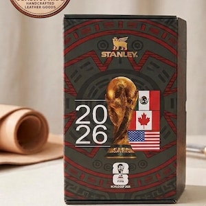 May include: A rectangular Stanley brand box featuring a dark green and red patterned design. The front displays the text 2026, a gold FIFA World Cup trophy graphic, the FIFA World Cup 2026 logo, and the flags of Mexico, Canada, and the United States.