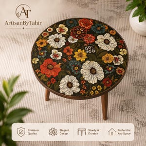 Può includere: Un tavolino rotondo in legno con sfondo scuro e un vivace motivo floreale di fiori bianchi, rossi, arancioni e gialli. Il tavolo ha tre gambe in legno affusolate e una superficie circolare liscia decorata con illustrazioni botaniche.
