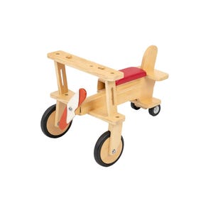 May include: A wooden ride-on toy shaped like an airplane with a natural light wood finish, a red seat, and a red and white propeller. The airplane features two large front wheels and two smaller rear wheels, all with black rubber tires.