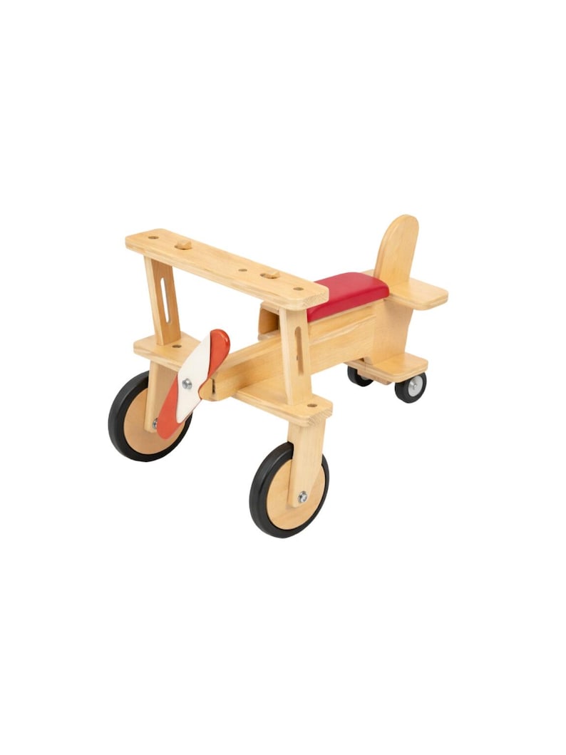 May include: A wooden ride-on toy shaped like an airplane with a natural light wood finish, a red seat, and a red and white propeller. The airplane features two large front wheels and two smaller rear wheels, all with black rubber tires.