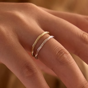 May include: Two thin, delicate rings worn on a finger. One ring is crafted from polished yellow gold, while the other is made of polished silver. Both bands feature a smooth, rounded profile and a simple, continuous circular design.