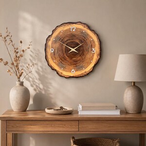 May include: A round wall clock crafted from a natural wood slice featuring visible tree rings, a dark brown bark edge, white numerals at the 12, 3, 6, and 9 positions, and thin gold-coloured metal clock hands centred on the wood grain surface.