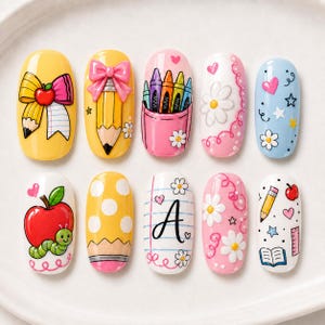 May include: Ten oval-shaped nail art press-on tips featuring school-themed designs including a pencil bow, a pencil with a pink bow, crayons in a pocket, daisies, hearts, a red apple with a green caterpillar, yellow polka dots, a letter A, and books.