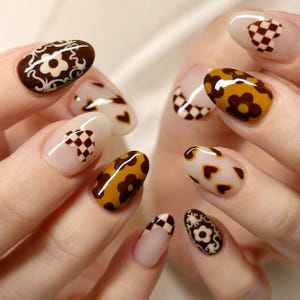 May include: Oval-shaped fingernails featuring a variety of nail art designs including brown and cream floral patterns, brown and tan checkered hearts, solid mustard yellow with brown flower accents, and brown and cream decorative scrollwork.