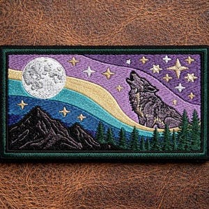 May include: A rectangular embroidered patch featuring a grey wolf howling at a white full moon. The scene includes a purple and blue night sky with yellow stars, a flowing light blue aurora, dark mountain silhouettes, and green pine trees.