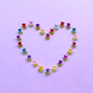 May include: A collection of small, glittery, translucent flower-shaped charms arranged in the shape of a heart. Each charm features a vibrant, multi-coloured resin flower head with a green stem and two leaves, showcasing a variety of colours.