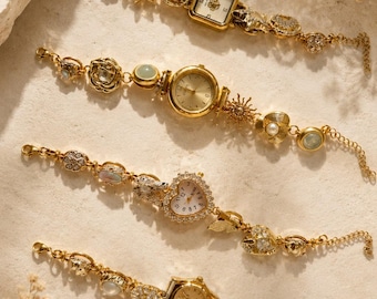 May include: Four gold-tone wristwatches with decorative link bracelets. The first has a square face, the second a round face with sun and shell charms, the third a heart-shaped face, and the fourth a round face with pearl-like accents.