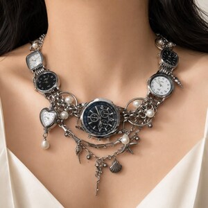 May include: A silver-toned statement necklace featuring multiple watch faces of varying shapes and sizes, including round and heart-shaped dials. The piece is accented with white faux pearls and small metallic charms shaped like seashells and starfish.