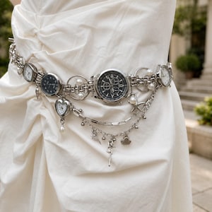 May include: A silver-toned chain belt featuring multiple watch faces, including a large central chronograph, a heart-shaped watch, and smaller round watches. The belt is adorned with white pearl beads, silver starfish, and seashell charms.
