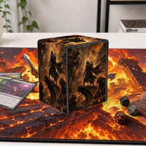 May include: A square deck box featuring a dark fantasy illustration of hooded figures standing on rocky terrain amidst a fiery landscape. The box is placed on a matching playmat with a lava theme, alongside several trading cards and dice.