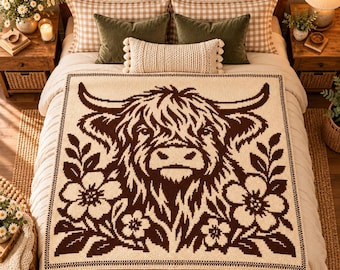 May include: A cream-colored knit blanket featuring a large, dark brown graphic of a Highland cow head centered between two floral arrangements. The design is framed by a simple border, showcasing a high-contrast, two-tone color scheme throughout.