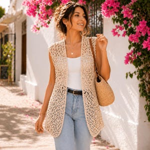 May include: A sleeveless beige crochet vest with an openwork pattern, worn over a plain white tank top and light blue denim jeans with a black belt. A woven straw handbag is carried on the shoulder, and a gold necklace with a pendant is worn.
