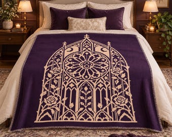 May include: A deep purple knit throw blanket featuring a cream-colored graphic design of a gothic arched window with a central rose window motif and climbing rose vines, finished with a whip-stitched edge detail along the sides of the blanket.