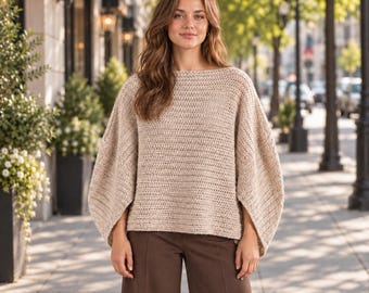 May include: A beige long-sleeved sweater with a boat neckline and wide, loose-fitting sleeves. The garment features a textured knit pattern throughout the body and sleeves, paired with solid dark brown trousers with a straight-leg cut.