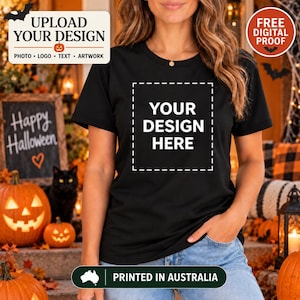 May include: A black short-sleeved t-shirt featuring a white dashed square outline and the text YOUR DESIGN HERE printed in white on the centre of the chest. The shirt is worn with light blue denim jeans, showcasing a simple and clean design.