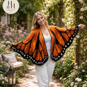 May include: A crochet butterfly wing shawl featuring a vibrant orange and black pattern with white accents along the scalloped edges. The garment is worn open, displaying a wing-like silhouette that drapes over the shoulders and arms.