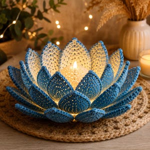 Puede incluir: Un portavelas de flor de loto hecho a ganchillo con pétalos superpuestos en tonos azules y blancos. El centro contiene una luz esférica texturizada y brillante que ilumina el intrincado patrón de puntos calados de los pétalos de hilo azul.