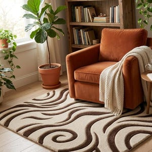May include: A rectangular area rug featuring a cream-colored base with dark brown, swirling, wave-like patterns. The rug is positioned on a light-colored wooden floor, partially underneath a burnt orange velvet armchair draped with a white throw.