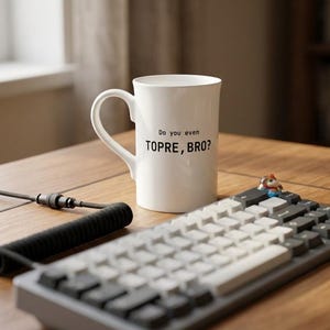 Puede incluir: Una taza de cerámica blanca con el texto impreso en negro Do you even TOPRE, BRO? La taza tiene un asa curva y está colocada junto a un teclado mecánico con teclas grises y blancas y un cable negro en espiral sobre una superficie de madera.