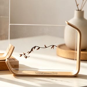 May include: Two clear acrylic display frames with light wood bases. The taller frame features a cartoon tiger sticker in a red bag. The shorter frame displays a delicate brown branch illustration and the text SereneCanvasmShop on the wood base.