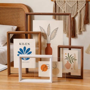 May include: A collection of four rectangular floating picture frames in wood and white finishes. The frames contain art prints featuring botanical illustrations, abstract shapes, and the text KILEN, displayed in a layered arrangement on a surface.