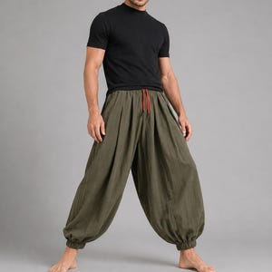 May include: A black short-sleeved t-shirt paired with loose-fitting olive green trousers. The trousers feature a gathered elastic waistband with a visible red drawstring and elasticated cuffs at the ankles, creating a voluminous silhouette.