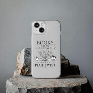 Könnte beinhalten: Eine transparente Handyhülle mit einer schwarzen Strichzeichnung eines offenen Buches mit Blumen, einer Kaffeetasse und einem Bücherstapel. Der Text lautet: BOOKS ARE MY escape REALITY IS MY PLOT TWIST, ergänzt durch kleine Sterne und ein Herz.