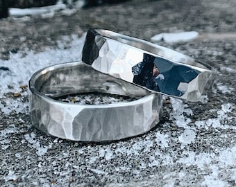 May include: Two silver hammered wedding bands stacked on top of each other on a wooden surface with snow on it.