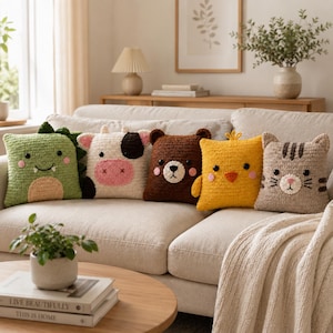 May include: Five square crochet pillows featuring animal designs: a green dinosaur with spikes, a white cow with black spots, a brown bear, a yellow chick with a small crest, and a beige cat with brown stripes, all with embroidered facial features.