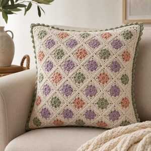 May include: A square crochet pillow cover featuring a diamond grid pattern. The design consists of cream-colored yarn with alternating floral motifs in soft shades of lavender, sage green, and peach. The edges are finished with a scalloped border.