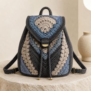 May include: A crochet backpack featuring a geometric pattern in shades of charcoal gray, light blue, and beige. The bag has a top handle, adjustable shoulder straps, a flap closure with a gold-tone metal accent, and a drawstring with gold-tone tips.
