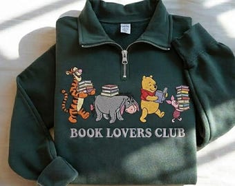 May include: A dark green quarter-zip sweatshirt featuring an embroidered graphic of Tigger, Eeyore, Winnie the Pooh, and Piglet carrying stacks of books. The text "BOOK LOVERS CLUB" is embroidered in white below the characters on the front chest.