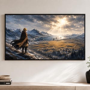 Op de afbeelding: Een ingelijste landschapsmuurkunstprint met een persoon in een bruine mantel die op een besneeuwde bergkam staat en uitkijkt over een uitgestrekte vallei met een dorp, een baai met schepen en verre besneeuwde bergen onder een zonnige lucht.
