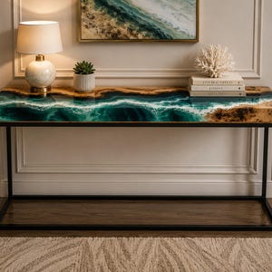 Puede incluir: Una mesa consola rectangular con un tablero de madera de borde natural y una incrustación central de resina que imita una ola oceánica turquesa con detalles de espuma blanca. La mesa se apoya en un marco de metal negro con base rectangular.