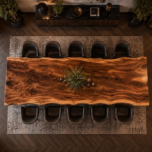 May include: A large rectangular dining table with a natural live edge wood grain surface, featuring a dark brown finish. Ten dark gray upholstered chairs are arranged around the table, with a small green plant centerpiece in the middle.