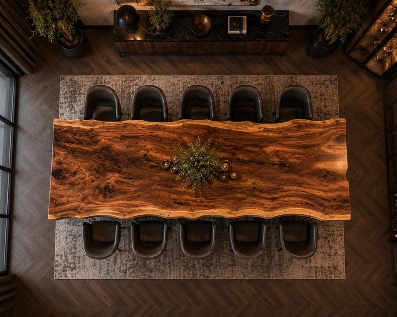 May include: A large rectangular dining table with a natural live edge wood grain surface, featuring a dark brown finish. Ten dark gray upholstered chairs are arranged around the table, with a small green plant centerpiece in the middle.