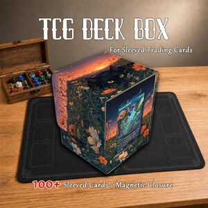 Op de afbeelding: Een TCG-deckbox voor kaarten met hoesjes en een magnetische sluiting, voorzien van een zwarte kat in een veld met oranje en witte bloemen bij zonsondergang. Een kaart is aan de voorzijde zichtbaar, naast een houten doos met gekleurde dobbelstenen.