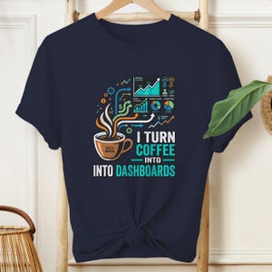 May include: A navy blue short-sleeve t-shirt featuring a graphic of a coffee cup with steam rising into various colorful data charts and graphs. The text reads I TURN COFFEE INTO DASHBOARDS, with the words DATA BREW printed on the coffee cup.
