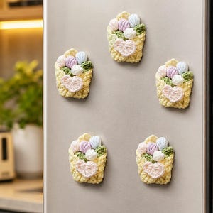 May include: Five handmade crochet flower bouquet magnets arranged in a pentagon shape. Each piece features a pale yellow crocheted basket holding small, textured flowers in shades of light pink, lavender, white, and green leaves.