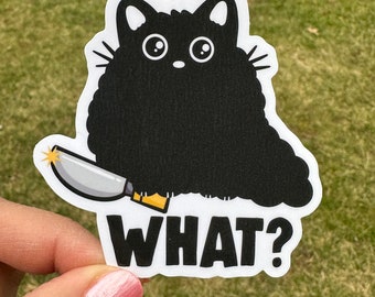 May include: A black cat sticker with a knife and the word "WHAT?" in bold, black letters. The cat has large, round eyes and a fluffy body. The knife is silver with a yellow handle.